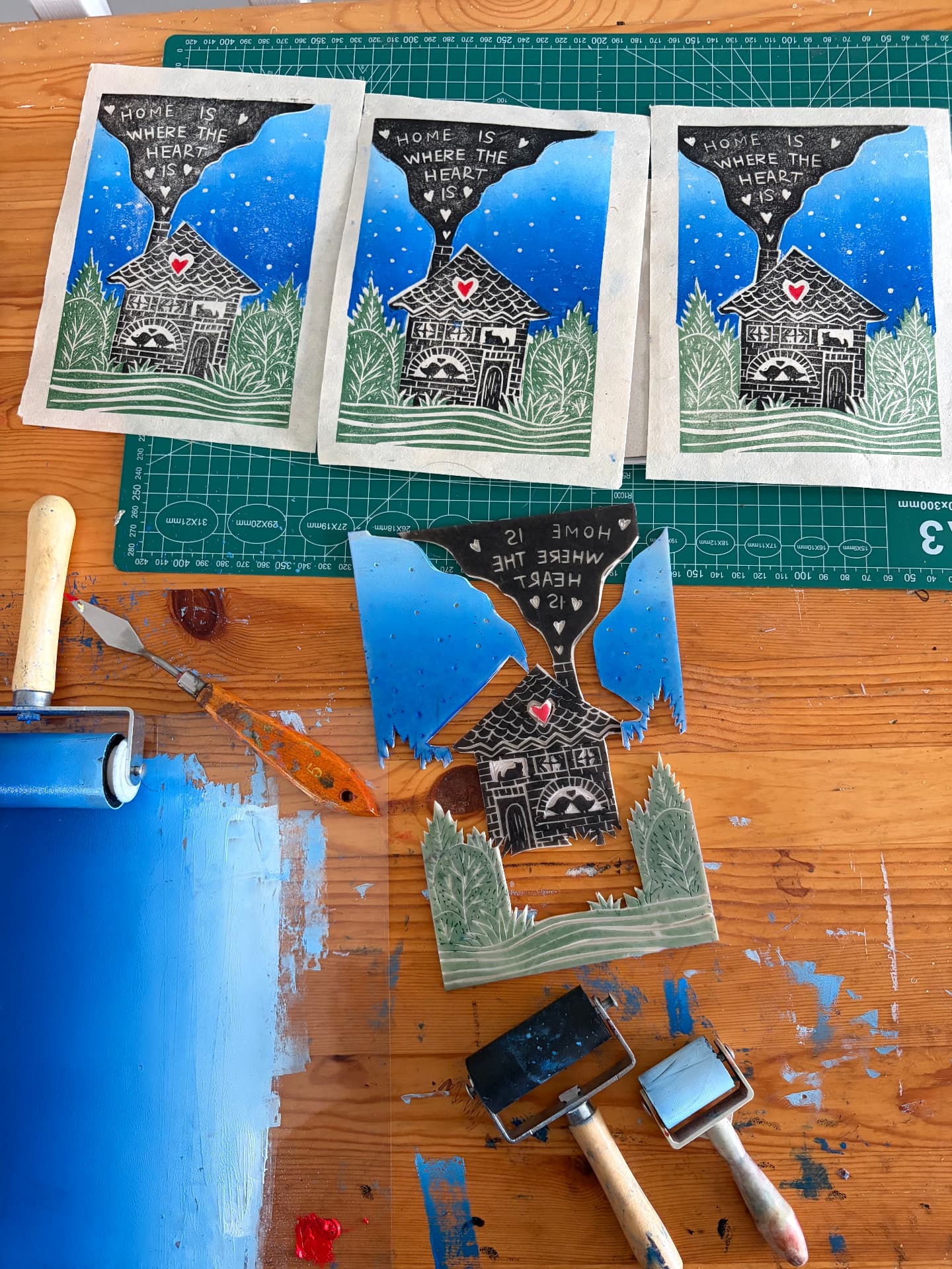 Three finished home is where the heart is lino prints, carved blocks, brayers and blue ink on a wooden studio table